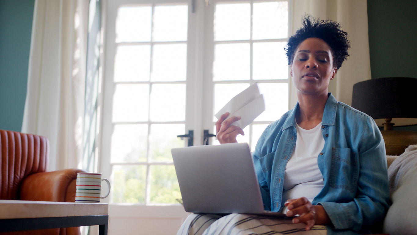 Menopausal Mature Woman At Home With Laptop Having Hot Flush Fanning Herself